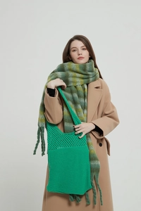 Dettaglio borsa a maglia verde traforata con sciarpa a frange su cappotto di lana