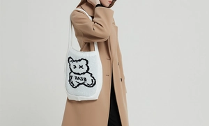 Close-up of white knitted tote bag with bear pattern worn with a camel wool coat
