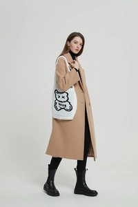 Close-up of white knitted tote bag with black cartoon bear print and BEAR lettering