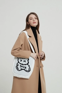 Close-up of white knitted tote bag featuring a black cartoon bear pattern and BEAR text