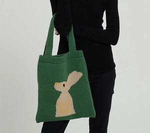 Dettaglio di una borsa tote in maglia verde scuro con motivo a coniglio beige indossata