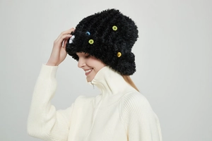 Detail einer schwarzen Plüsch-Strickmütze mit bunten Zierknöpfen auf grauem Hintergrund