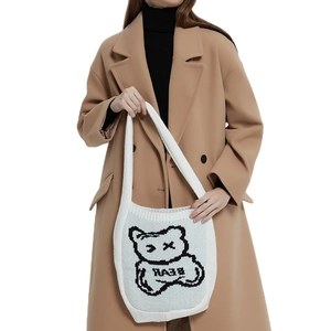 White knit tote bag with black bear pattern worn with a camel coat on a white backdrop