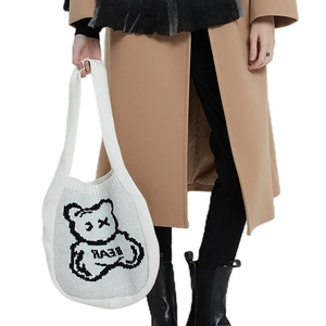 White knit tote bag with a cartoon bear design held by a model in a wool coat