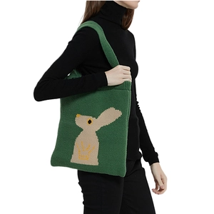 Borsa tote in maglia verde con motivo a coniglio beige indossata da modella in abito nero
