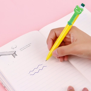 Penna a sfera gialla a scatto con clip a rana verde scrivendo su un taccuino rosa