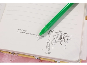 Nahaufnahme eines grünen Gelschreiber auf einem linierten Notizbuch mit Katzenmotiven