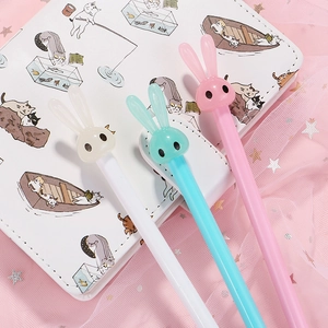 Three cute long-eared bunny gel pens in pastel colors on a stylish notebook background