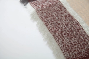 Detalle de bufanda de punto a cuadros burdeos y grises con textura suave y flecos
