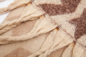 Detailansicht der beigen und braunen Stricktextur mit gewebten Fransen und Quasten