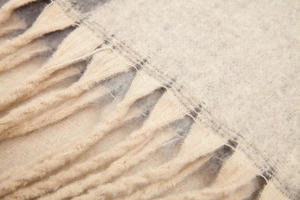 Close-up of thick beige knit shawl showing soft bouclé texture and long fringe tassels