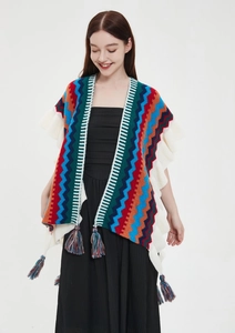 Dettaglio di poncho in maglia colorata con motivi etnici e nappine con frange