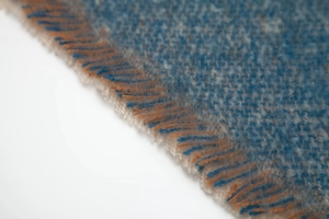 Detailed macro view of woven grey-blue shawl with orange and blue fringe tassels