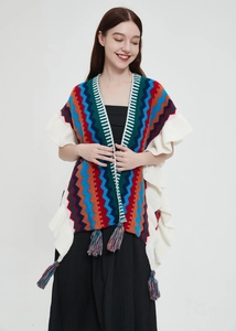 Dettaglio di un poncho in maglia etnica con motivi a onde colorate e bordi con volant bianchi