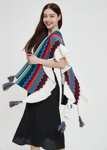 Dettaglio di uno scialle in maglia boho con motivi a onde colorate e bordi con frange bianche
