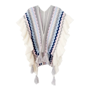 Dettaglio di un poncho in maglia con motivi zigzag, bordi a balze e nappe grigie appese