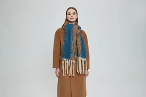 Detail of chunky knit scarf with blue pattern and long white tassels on camel coat