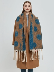 Close-up of caramel thick knit scarf featuring blue polka dots and chunky tassels
