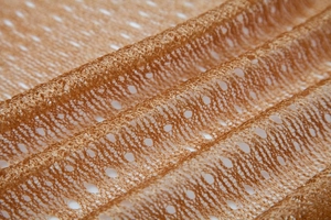 Detail of orange gold hollow mesh fabric with intricate geometric knit and tassel texture