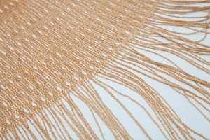 Close-up of golden hollow-out knit shawl featuring intricate mesh pattern and tassel fringe