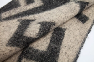Détail de l'écharpe en maille beige montrant la texture bouclée et le motif jacquard F