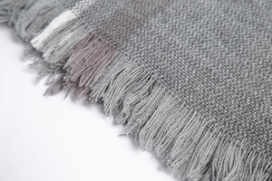 Close-up of grey knit scarf with fine fringe detailing and soft purple stripe patterns