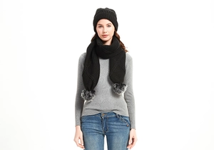 Detailaufnahme des schwarzen Stricksets aus Schal und Mütze mit grauen Kunstfellbommeln