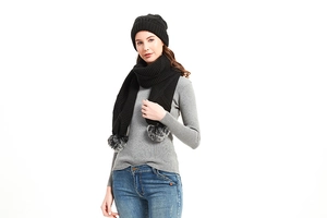 Detail eines schwarzen Stricksets aus Mütze und Schal mit flauschigen Kunstfellbommeln