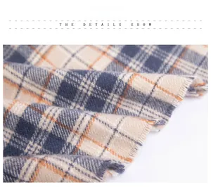 Close-up of navy, beige and orange plaid scarf showing soft fabric and tassel edge