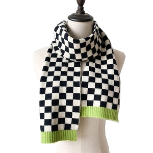 Detail of checkered knit scarf with neon green ribbed edges on a white background
