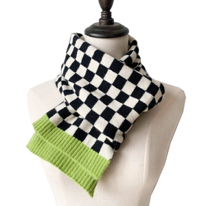 Detail of checkered knit scarf featuring black-white pattern and green ribbed edge