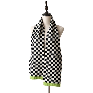 Detail of checkered knit scarf featuring black and white pattern and green ribbed hem