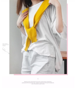 Detail of a bright yellow knitted shoulder wrap layered over a white casual outfit