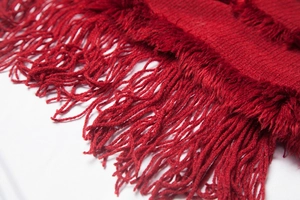 Detail of red knit shawl featuring long fringe tassels and soft textured fabric weave