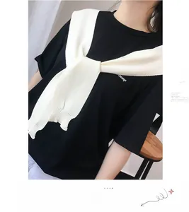Detail view of a white knitted shoulder wrap styled over a minimalist black branded T-shirt