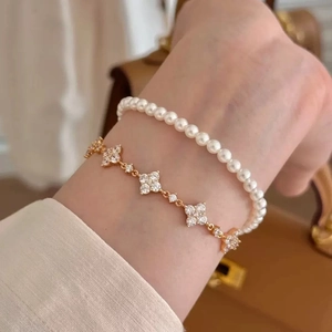 Detail von geschichtetem Gold-Kleeblatt-Armband und Perlenarmband am Handgelenk