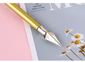 Close-up of gold calligraphy pen with pointed silver nib on a pink floral background