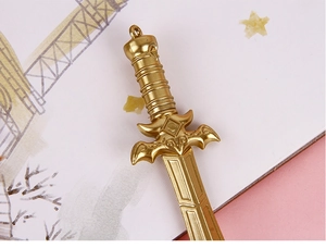 Close-up of golden sword-shaped pen pendant featuring intricate fantasy engraving