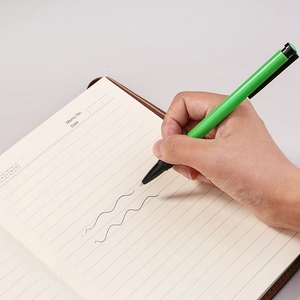 Green retractable ballpoint pen with black grip writing on a lined notebook in blue ink