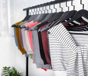 Row of colorful knitted shawl wraps hanging on hangers against a white wall background