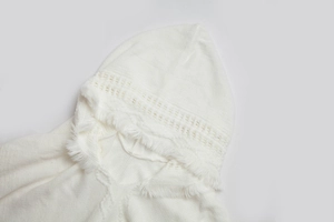 Detail eines weißen Strickponchos mit hohlem Netzmuster und Fransen an der Kapuze