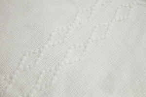 Nahaufnahme des weißen Strickponchos mit klassischem Zopfmuster und Rautenstruktur