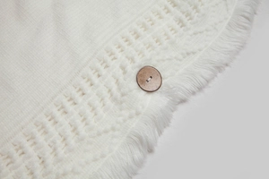 Detail eines weißen Strickschals mit hohlem Netzmuster, Fransen und Holzknopf