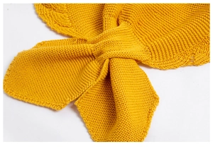 Close-up of ginger yellow knit shawl featuring a cross-over design and woven texture