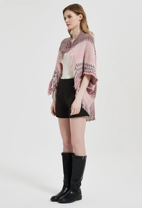 Détail d'un poncho en tricot rose avec motifs à rayures ondulées et pompons à franges chic