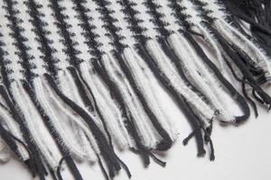 Makro-Detail des Hahnentritt-Strickmusters und feiner Fransenkanten am Schal