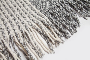 Close-up of the grey and white striped knit texture and fringe tassels of the poncho