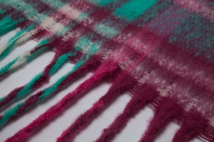 Close-up of magenta and teal plaid scarf with thick mohair yarn texture and long tassels