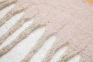 Detailopname van dikke gebreide sjaal met roze en beige mohair textuur en lange kwastjes