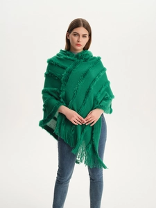 Detail view of dark green knitted poncho with textured stripes and long fringe trim